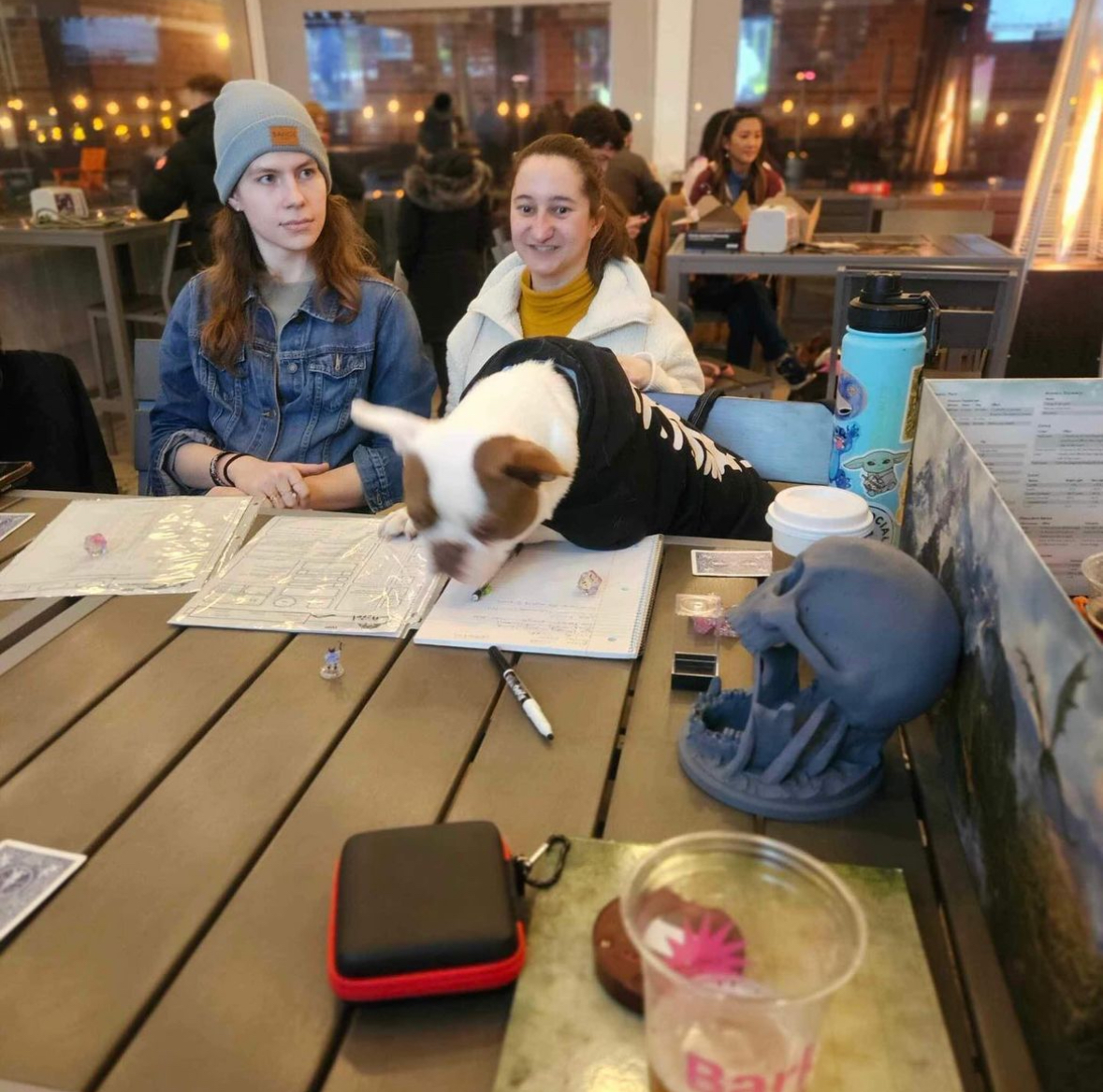 A photo from Bark Social. It features a French Bulldog named Stitch overlooking a table of assorted D&D items. Two players are seated at the table behind the dog.